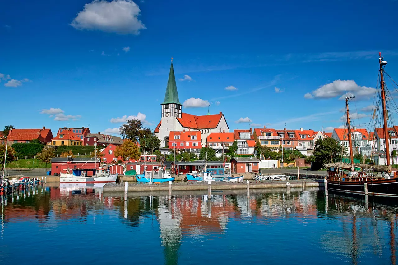 A picturesque harbour in Ronne, Denmark, showcasing colourful boats and a charming church tower against a clear blue sky | MSC Cruises